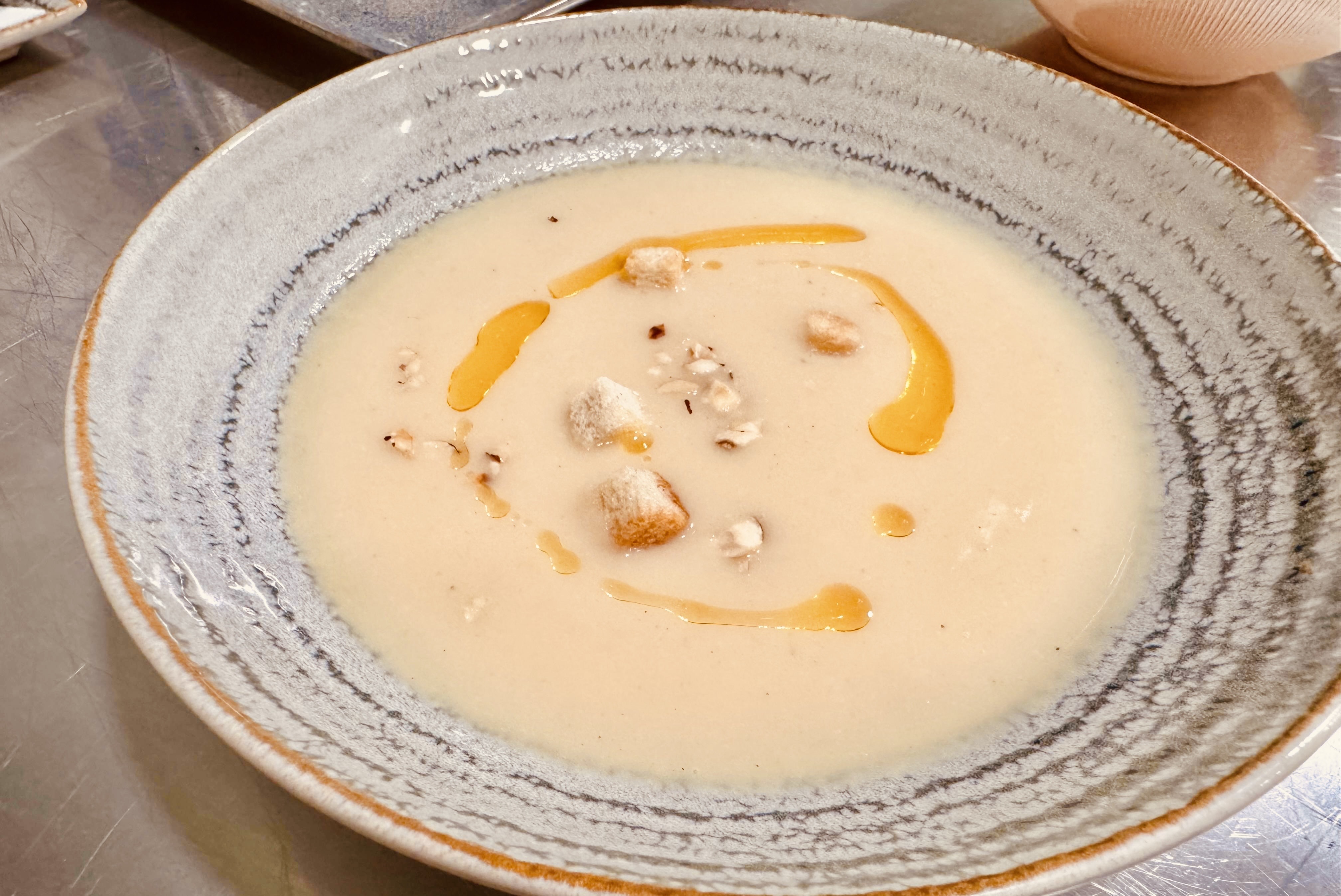 Cream soup with croutons and golden oil drizzle in artisan ceramic bowl